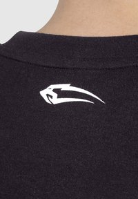 T-shirt en coton noir avec un col rond ; présente un logo blanc stylisé près du col. Texture douce avec un design classique.