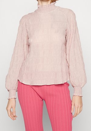 Faltenbluse in hellrosa mit langen Ärmeln, hohem Rüschensaum und elastischen Ärmeln, kombiniert mit gerippten rosa Hose.