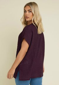 Lila texturerad topp med korta ärmar och avslappnad passform, med en lägre fåll och sidoklyftor, i kombination med blå jeans.