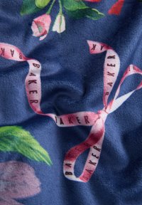 Tessuto floreale con sfondo blu navy, superficie testurizzata e un nastro in raso rosa con la scritta "BAKER" in nero, annodato in modo lasco.