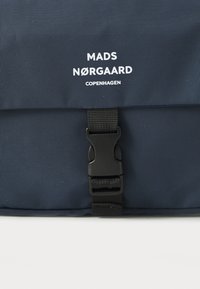 Navyblaue Tasche aus strukturiertem Stoff, mit einem Magnetverschluss und dem auf der Vorderseite aufgedruckten weißen Logo "MADS NØRGAARD KOPENHAGEN".