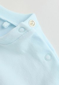 Vêtement pour bébé bleu clair avec boutons-pression sur la zone des épaules, présenté en gros plan sur un fond blanc.