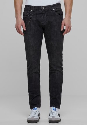 Musta farkut, joiden istuvuus on slim fit, sivuketjuyksityiskohdalla, viiden taskun suunnittelulla ja hienovaraisella tekstuurilla. Yhdistettynä valkoisiin ja harmaisiin tennareihin.