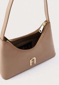 Mala de mão em couro castanho com design curvo, ferragens douradas e fecho de correr. Apresenta um bolso interior e uma etiqueta com o logótipo no interior.