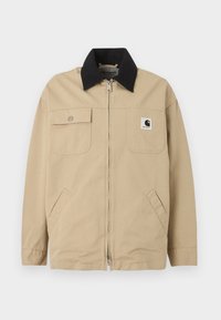 Μπεζ ζακέτα με φερμουάρ, μαύρο γιακά, αριστερή τσέπη στο στήθος, δεξιά τσέπη με καπάκι και κουμπί στο στήθος, και πλαϊνές τσέπες.