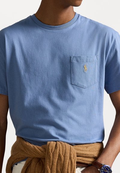 Tricou de bumbac de culoare albastru deschis, cu guler rotund, mâneci scurte și un buzunar pe piept ce prezintă un mic logo brodat. Pulover din tricot cu textură legat în jurul taliei.