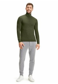Grüner langärmeliger Rollkragenpullover kombiniert mit hellgrauen Jogginghosen. Schlichtes Design, taillierte Form und weiche Textur. Weiße Sneakers runden das Outfit ab.