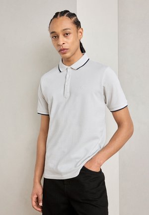 Polo shirt gris clair à manches courtes avec une patte de boutonnage et une touche de marine sur le col. Tissu texturé avec un branding subtil.