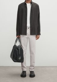 Czarna koszula zapinana na guziki, biała koszulka, jasnoróżowe spodnie, czarna skórzana torba i czarne buty; gładka tekstura i prosty design w całym zestawie.