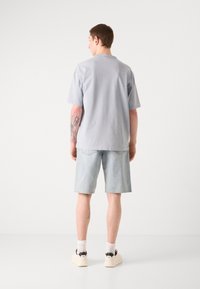 Lys grå kortærmet t-shirt, afslappet pasform, parret med lyseblå denimshorts og hvide sneakers med sorte accenter.