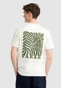 Crème-kleurig katoenen t-shirt met een groot groen abstracte draai ontwerp op de achterkant en het woord "FARAH" in vet eronder.