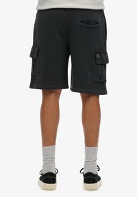 Pantalones cortos de carga negros hechos de tela texturizada, con múltiples bolsillos, un corte relajado y longitud hasta la rodilla. Combinados con calcetines grises y zapatos negros.
