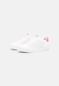 Bílé sportovní boty s síťovaným designem, vybavené pevným gumovým podešví, růžovými akcenty na patě a logu, a šněrováním.