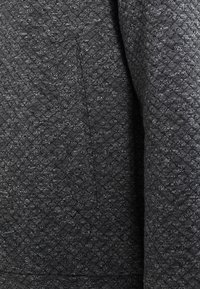 Gestructureerde, donkergrijze stof met een diamanten patroon, met een gladde afwerking en subtiele variaties in schaduwen. Geschikt voor kleding.