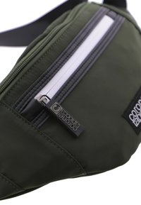 Riñonera de color verde oliva, resistente al agua, fabricada con un tejido de textura suave, con un zipper blanco y una etiqueta de logo negra.