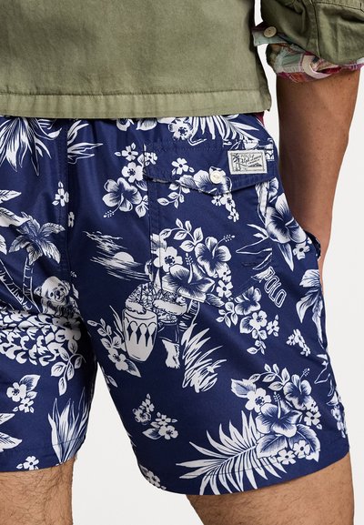 Shorts de bain bleus à motifs floraux blancs tropicaux, avec un logo brodé et une poche arrière. Le matériau semble léger et lisse.