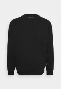 Felpa nera con maniche lunghe, scollo tondo e polsini a costine. Presenta un piccolo logo bianco sulla parte posteriore vicino al collo. Texture morbida.