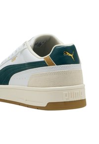 Sneaker bianco con accenti verdi e crema, dotato di un tallone in suede testurizzato, suola in gomma e logo Puma dorato sul retro.