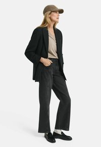 Sort blazer over en beige v-neck top, parret med mørkegrå brede ben-jeans. Accessoriseret med en brun kasket og sorte loafers.
