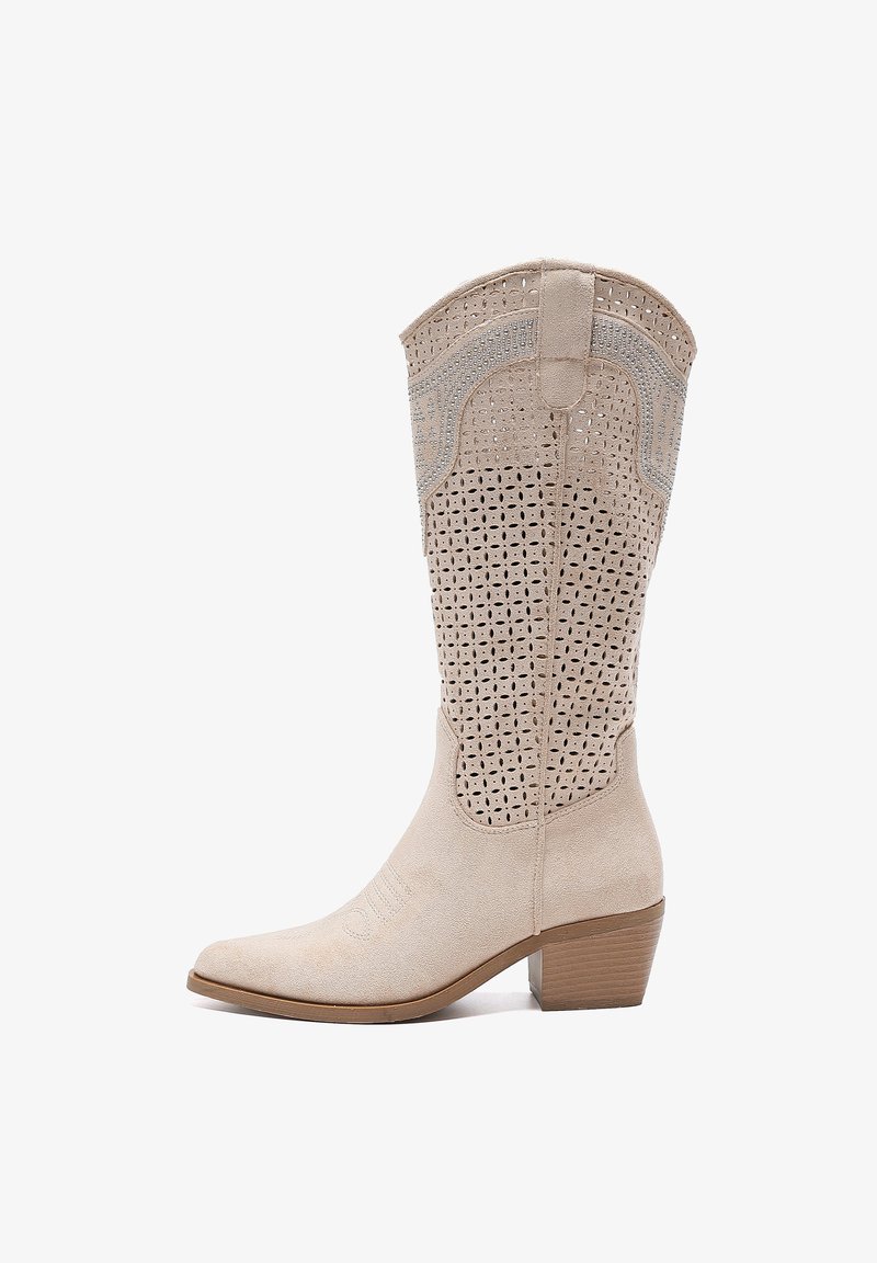 Botas de vaquero de gamuza beige con un patrón de corte decorativo, punta afilada y tacón apilado. Presenta un detalle de costura a lo largo del costado.