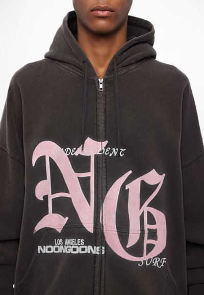 Sweat à zip noir avec de grandes lettres graphiques roses "N" et "G" et le texte "LOS ANGELES NOONGOONS SURF". Tissu doux et texturé.
