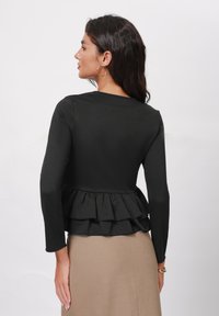 Top negro con peplum, de mangas largas y con un dobladillo con volantes, que presenta una textura suave. Combinado con una falda ajustada de color marrón claro.