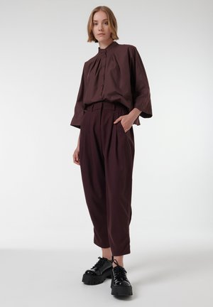 Blusa color marrón con un cuello alto y cierre de botones en la parte delantera, combinada con pantalones holgados marrones y zapatos de plataforma negros. Textura suave, ajuste relajado.