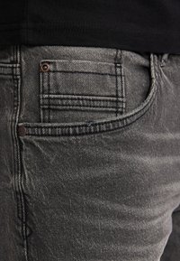 Zwarte spijkerbroeken van denim met een vervaagde textuur, vijf-pocket ontwerp en een koperen knop. Stikdetails zijn zichtbaar langs de naden.