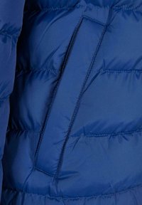 Marineblå dynejakke stof med quiltet design, der har en sidelomme med låg og glat tekstur.