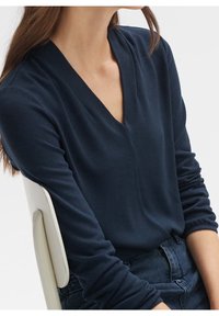 Námořnická modrá svetr s výstřihem do V vyrobený z měkké, strukturované tkaniny s dlouhými rukávy, s volným střihem a žebrovanými manžetami.