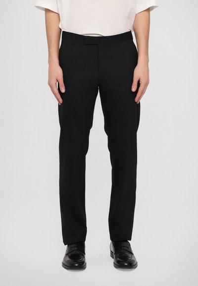 Pantalones negros de corte ajustado con una textura suave, estilo slim fit y diseño de frente plano. Combinados con una camisa de color claro y zapatos negros.