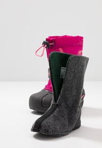 Botas de nieve de tamaño infantil con una parte superior de color rosa brillante, cordón de plástico y suela de goma negra. El forro interior extraíble es gris con tejido verde.
