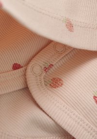 Różowa, pr�ążkowana tkanina z małymi wzorami truskawek. Ma zatrzaski i miękką fakturę. Skupienie na dekolcie i detalach ubrania.
