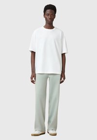 Hvid kortærmet T-shirt med løs pasform, parret med lysegrønne brede bukser. Minimalistisk design, blødt stof med en glat tekstur.
