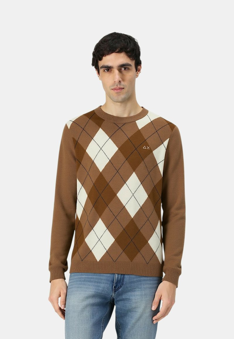 Maglione a motivo argyle marrone con diamanti color crema, collo rotondo e polsini a costine. Indossato sopra dei jeans blu, con un piccolo logo sul petto.