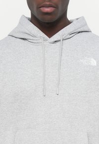 Hanorac gri cu glugă, realizat dintr-un amestec de bumbac, având un buzunar frontal și șnururi. Logo-ul The North Face este brodat pe partea stângă a pieptului.