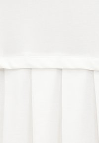 Λευκό ύφασμα με πιετέ σχέδιο και οριζόντιο ράμμα κοντά στην κορυφή, που δείχνει υφή και φωτεινές σκιές.