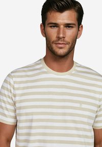 Gestreiftes T-Shirt mit abwechselnden beige- und weißen Streifen, rundem Halsausschnitt und kurzen Ärmeln. Weicher Stoff mit einem dezenten Logodetail.