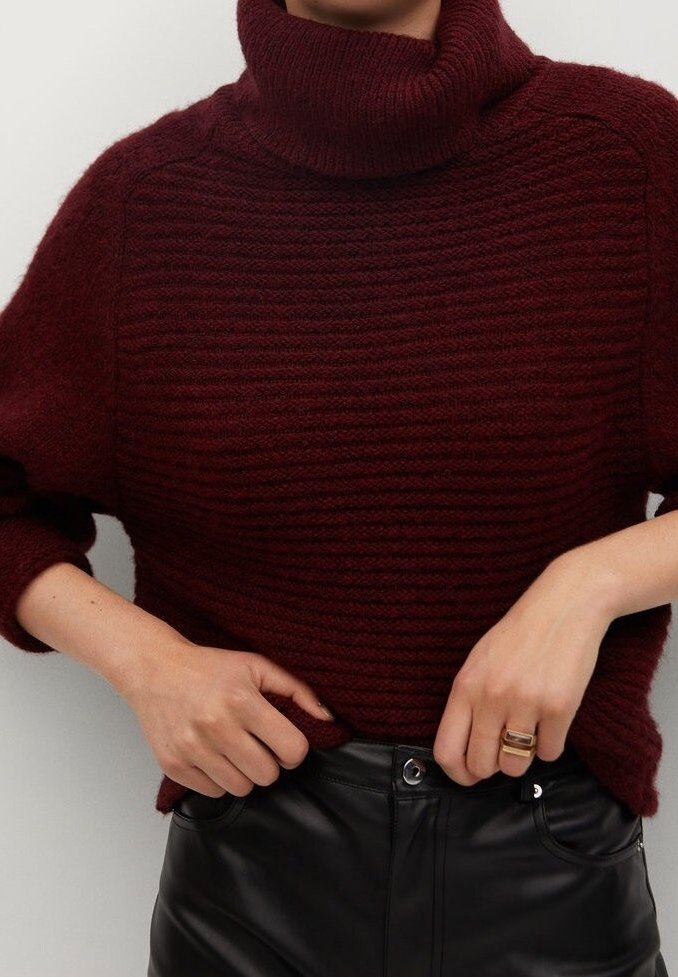 Burgundy neulepaita, jossa on korkea kaulus, ribatoitu pinta ja laskeutuvat olkapäät, yhdistettynä mustiin nahkahousuihin.