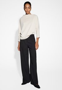 Top drappeggiato beige chiaro con scollatura a barca, abbinato a pantaloni neri a gamba larga. Tessuto liscio, cuciture minime e nessun motivo visibile.