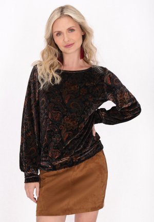 Top in velluto nero con maniche lunghe e intricate fantasie paisley arancioni e marroni, abbinato a una mini gonna in suede marrone.