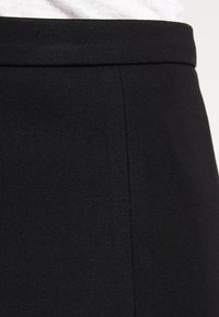 Jupe en tissu stretch noir avec une texture lisse, dotée d'une large taille élastique et de lignes épurées, convenant à diverses occasions.