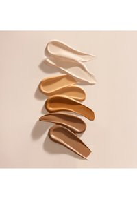 Fünf flüssige Foundation-Proben in verschiedenen Schattierungen von Beige, Braun und Creme, mit glatten, glänzenden Texturen vor neutralem Hintergrund.