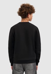 Zwarte sweatshirt met een ronde hals, ribbelmanchetten en -zoom, gemaakt van zachte stof. De achterkant toont een eenvoudig ontwerp zonder versieringen.