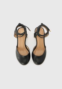 Schwarze Leder-High-Heel-Sandalen mit Knöchelriemen, abgerundeten Zehen und beigen Innensohlen. Das Riemendetail verfügt über goldene Akzente für zusätzlichen Stil.