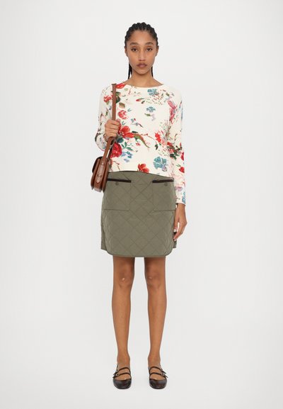 Pull en tricot fleuri cr�ème, jupe matelassée verte avec poches et sac à bandoulière marron. Le modèle porte des ballerines noires.
