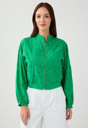 Giacca verde con zip, decorata con motivi floreali ritagliati, maniche lunghe e collo alto. Il tessuto sembra leggero e presenta una leggera texture.