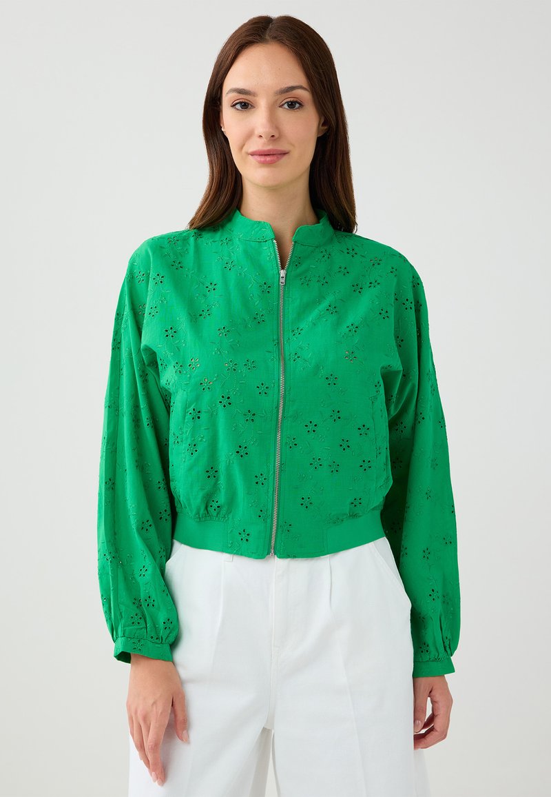 Groene ritsjack met florale uitsnijdingen, lange mouwen en een hoge hals. Stof lijkt lichtgewicht met een lichte textuur.