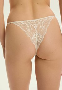 Ivory Spitze-Tanga mit floralem Muster, ausgestattet mit einer zarten Textur und fransigen Kanten, entworfen für minimale Rückendeckung.