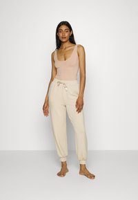 Jasno beżowy top na ramiączkach z okrągłym dekoltem w połączeniu z jasnymi kremowymi spodami dresowymi z elastycznym paskiem i mankietami, wykonanymi z miękkiego, gładkiego materiału.